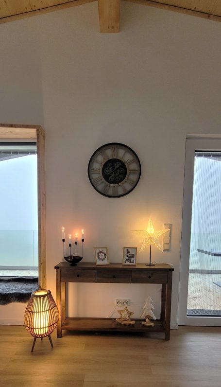 Rustikales Zimmer mit Uhr, Holztisch, Kerzen und Fensterblick auf das Meer.